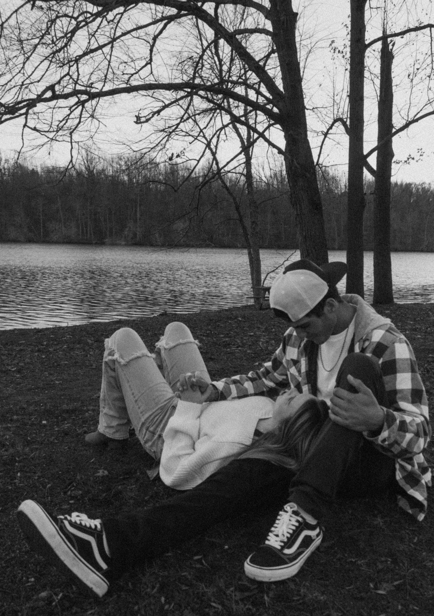 Person relaxing by a lake wearing plaid and sneakers in black and white.