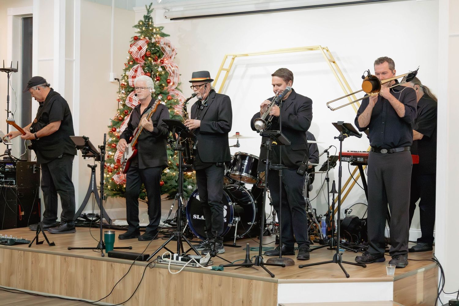 A live band performs holiday music on stage near a decorated Christmas tree at a festive indoor event.