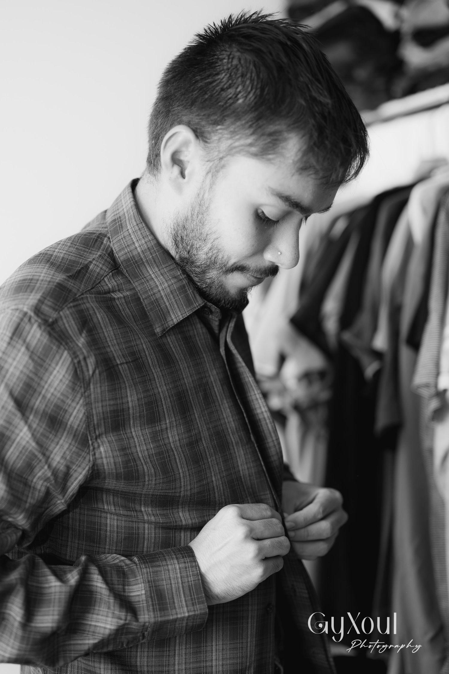 Black and white portrait of person buttoning plaid shirt.