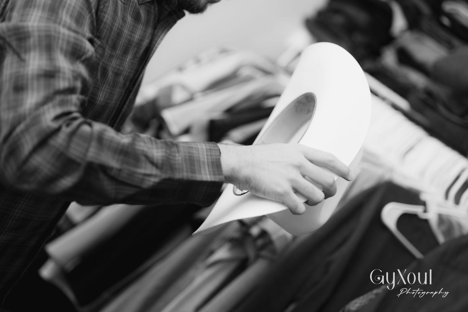 Close-up black and white photo of hands sorting through hanging clothes.