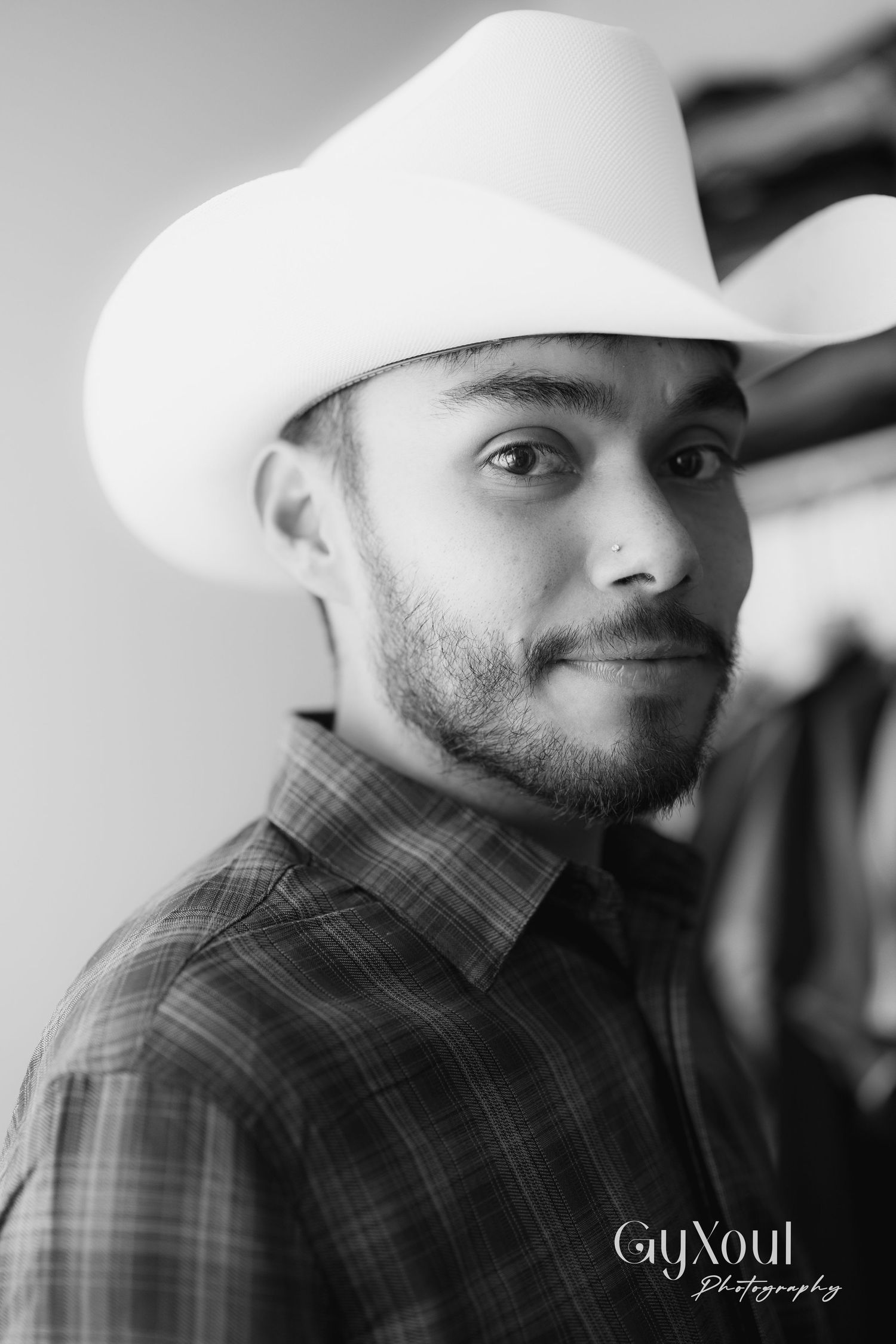 Portrait of person wearing white cowboy hat and plaid shirt in black and white.