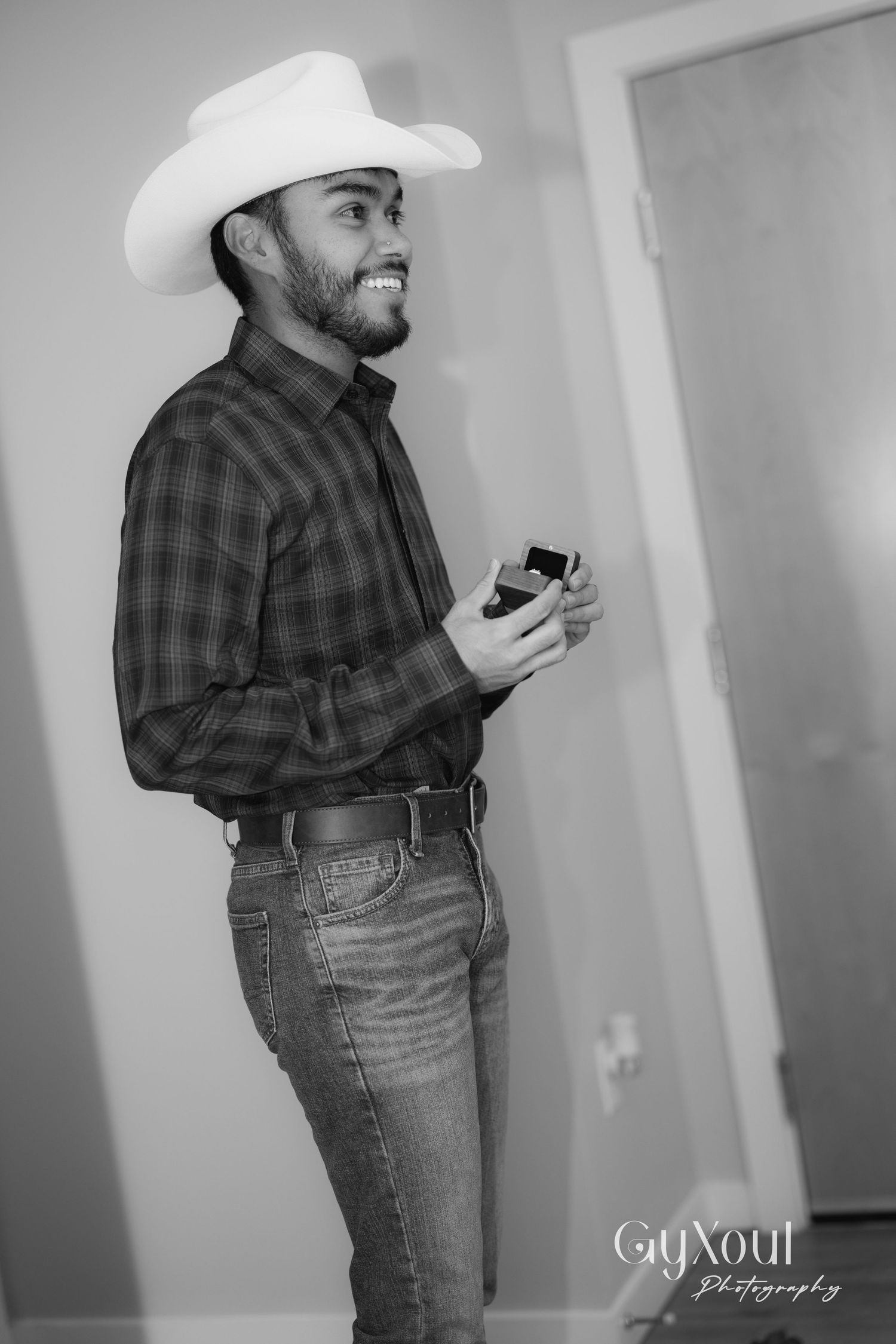 Man in plaid shirt and cowboy hat holding small box and smiling.
