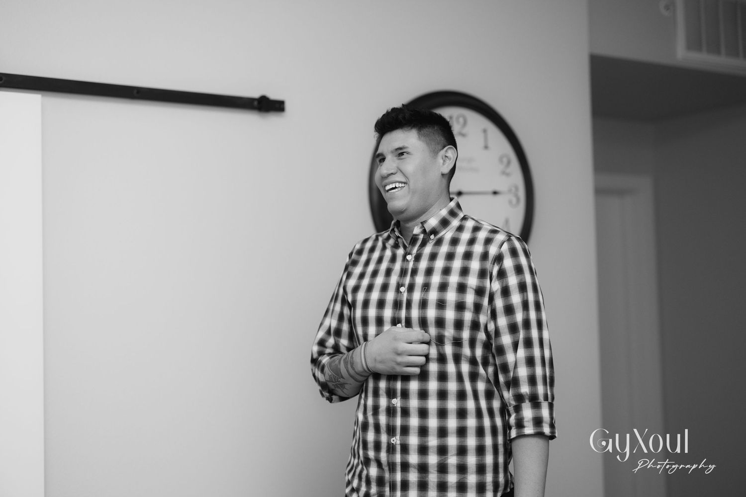 Person in checkered shirt laughing indoors with white walls.