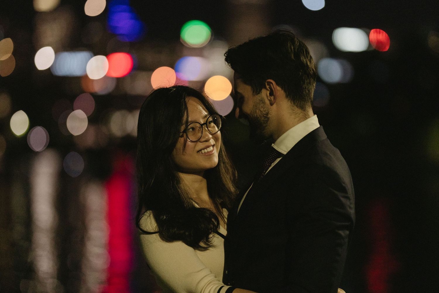 A romantic couple embraces in silhouette against a blurred background of colorful bokeh lights.