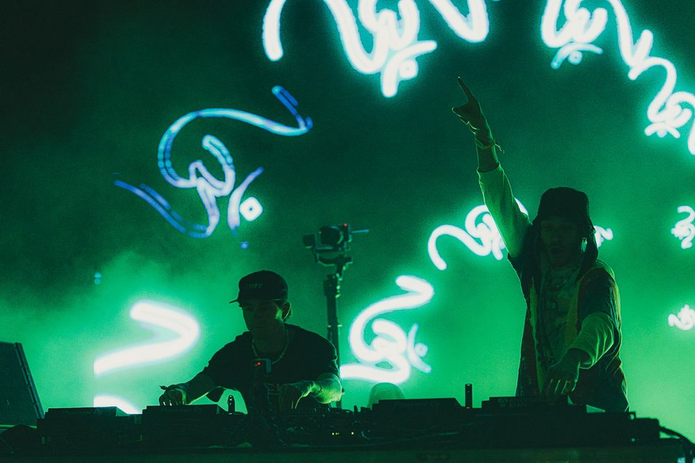 Silhouetted performers on stage with bright neon green lighting effects creating a dramatic concert atmosphere.