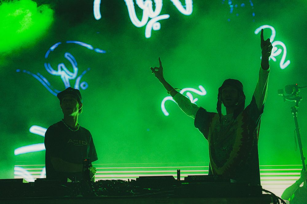 Concert performers in silhouette against a vibrant green light show backdrop during a live performance.