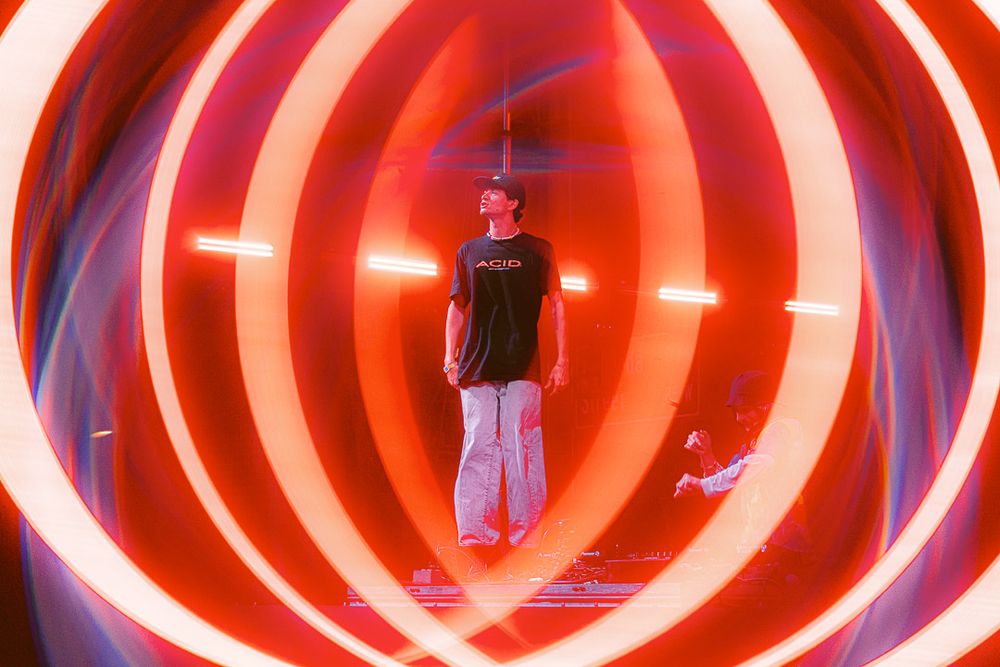 Performer silhouetted against concentric red neon circles on stage.