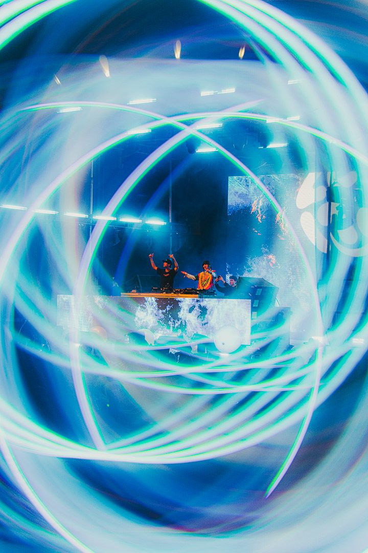 Abstract blue and white light trails create a spiral tunnel effect during a live performance.
