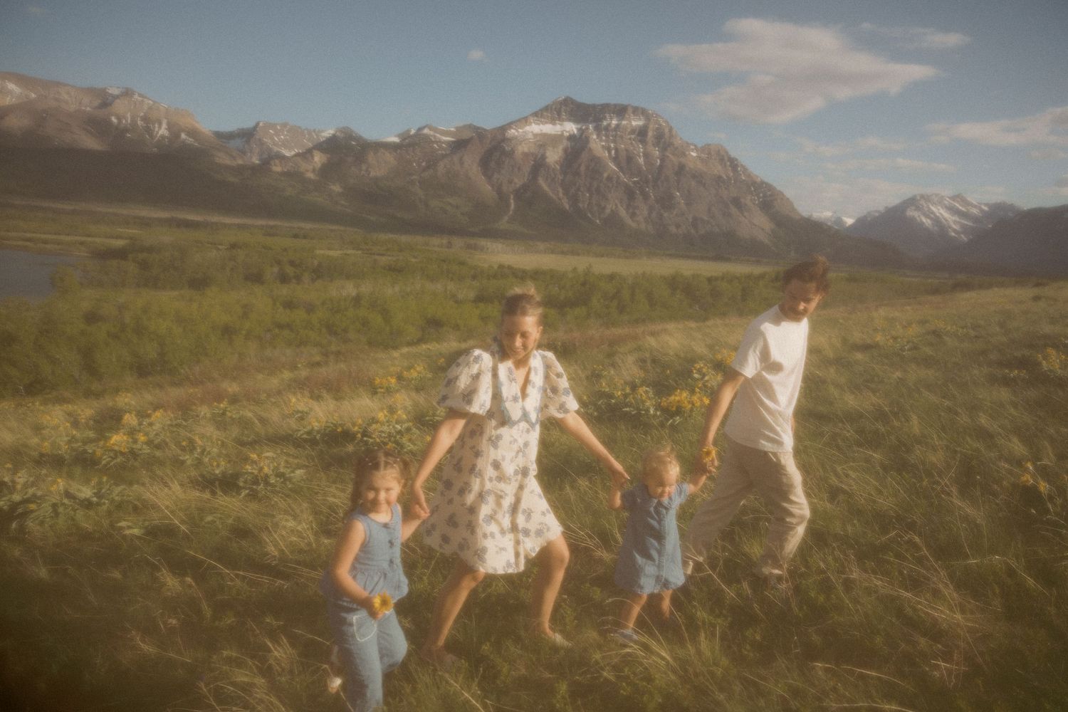 Family members jump and play together in a scenic mountain meadow during golden hour.