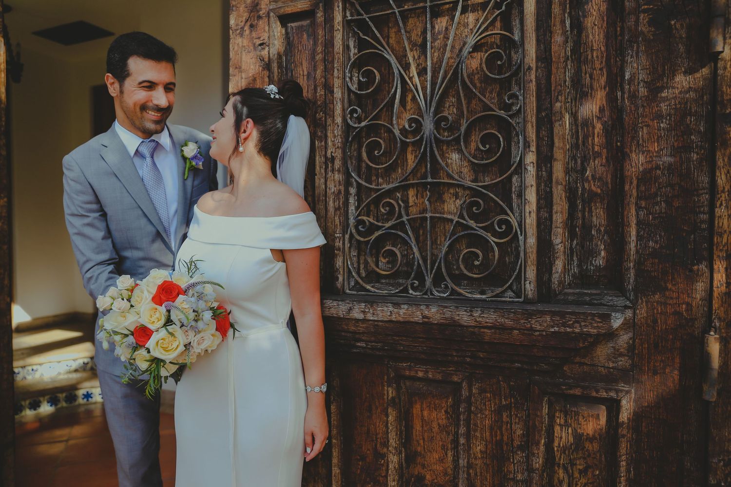 A bride and groom share an intimate moment in front of ornate wooden doors with decorative ironwork.Pedregal Los Cabos Wedding Photographer