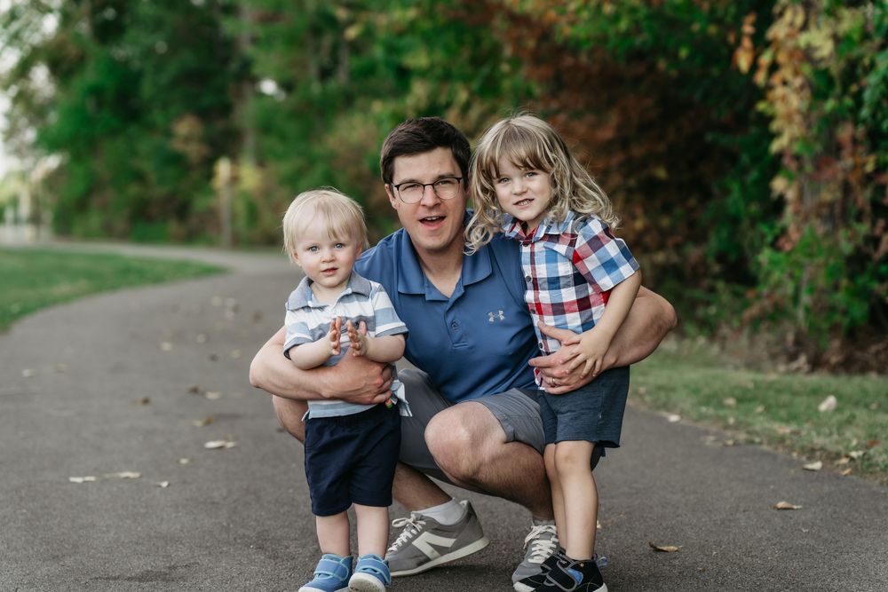A group sits together on a paved path surrounded by lush greenery during a casual outdoor photo session at Delaware, Ohio Family Photo Sess