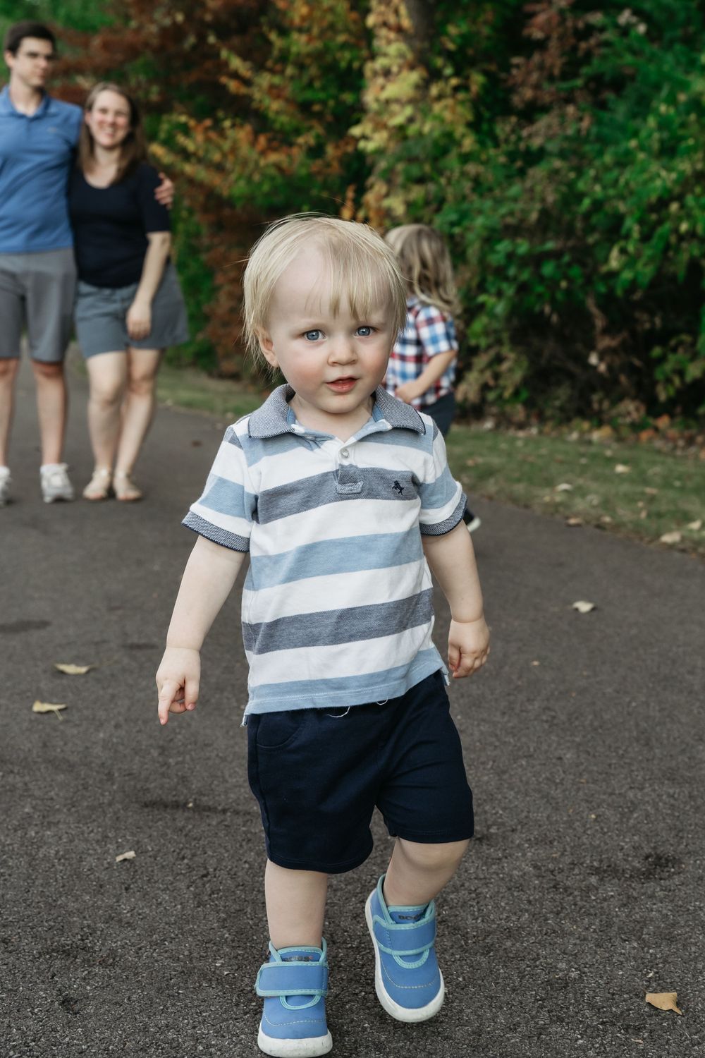 Small child wearing striped polo shirt and navy shorts walks on paved path in Delaware, Ohio Family Photo Session