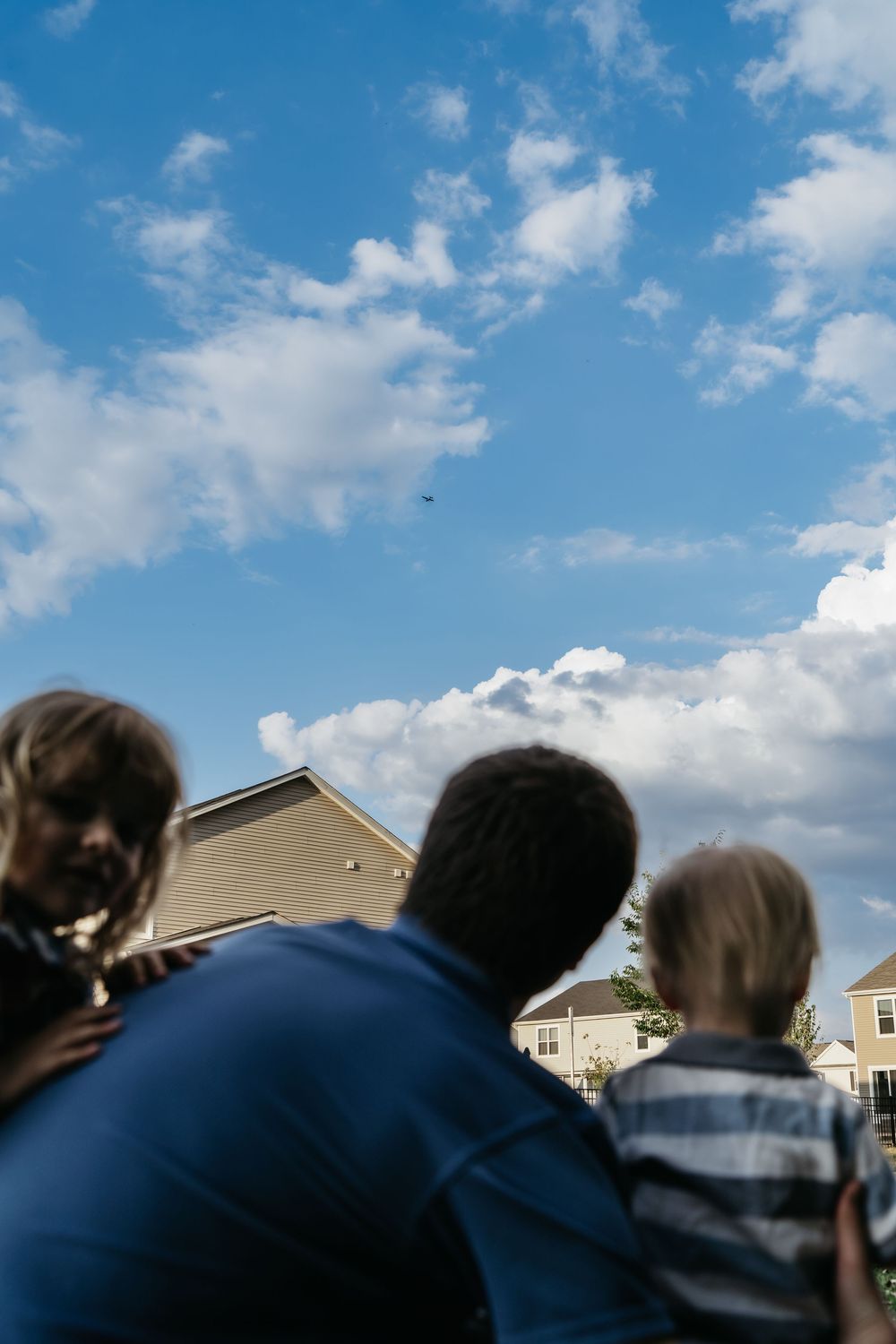 A series of silhouetted figures stand against a bright blue sky with white puffy clouds and suburban houses in the background for Ohio Photo
