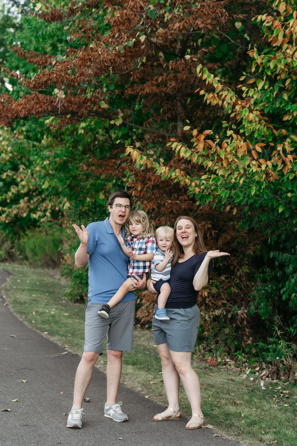A family poses playfully together on a path with autumn foliage in the background in Delaware, Ohio for a Family Photo Session