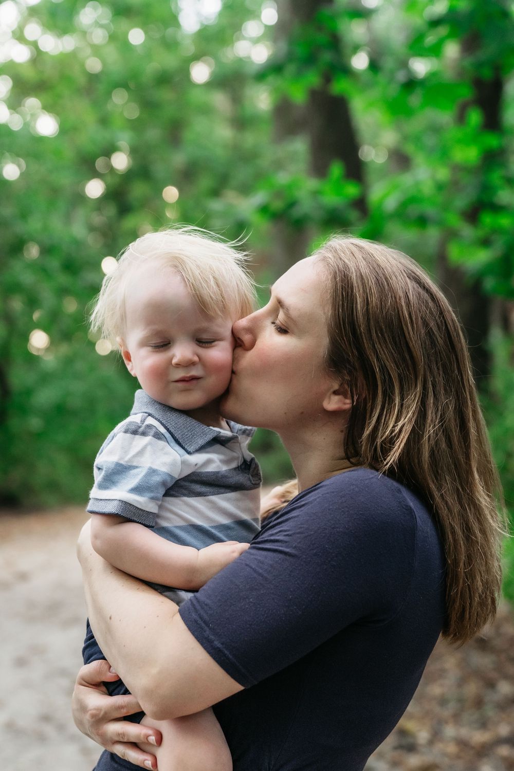 A tender moment of affection and bonding captured in a natural outdoor setting with green foliage in Delaware, Ohio Family Photo Session