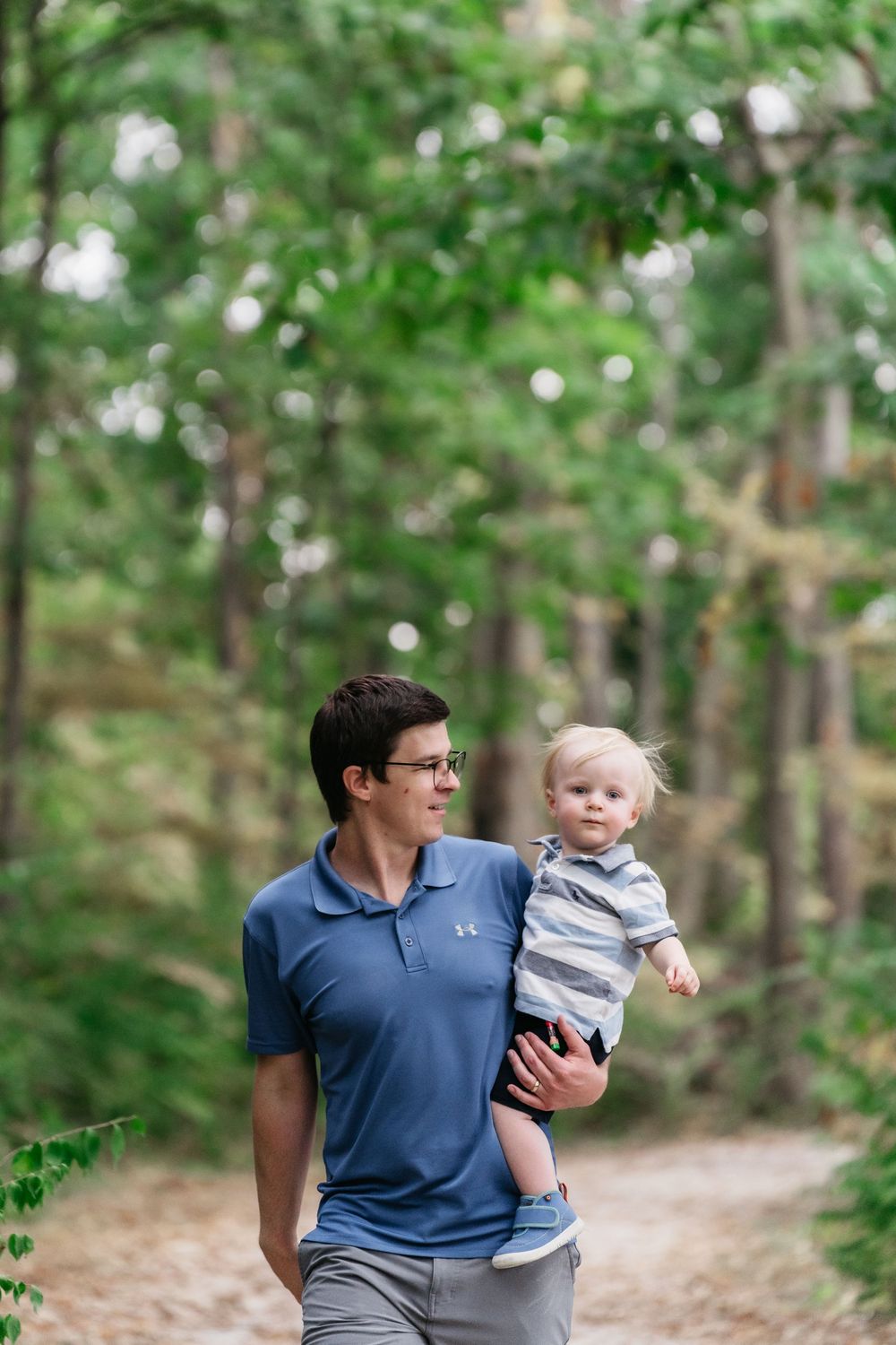 Parent and child share a tender moment while walking through a sunlit wooded path on a summer afternoon in Delaware, Ohio for family photos