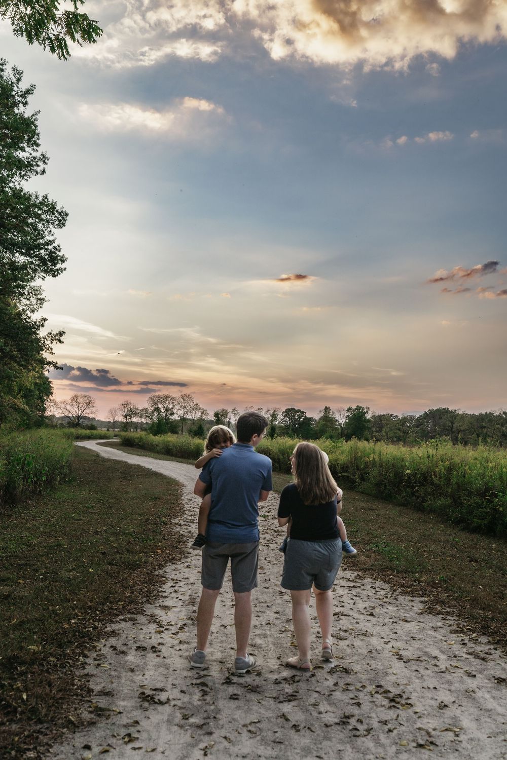 A group walks together along a sandy path at sunset with dramatic clouds and trees in the background in Delaware, Ohio family photo session