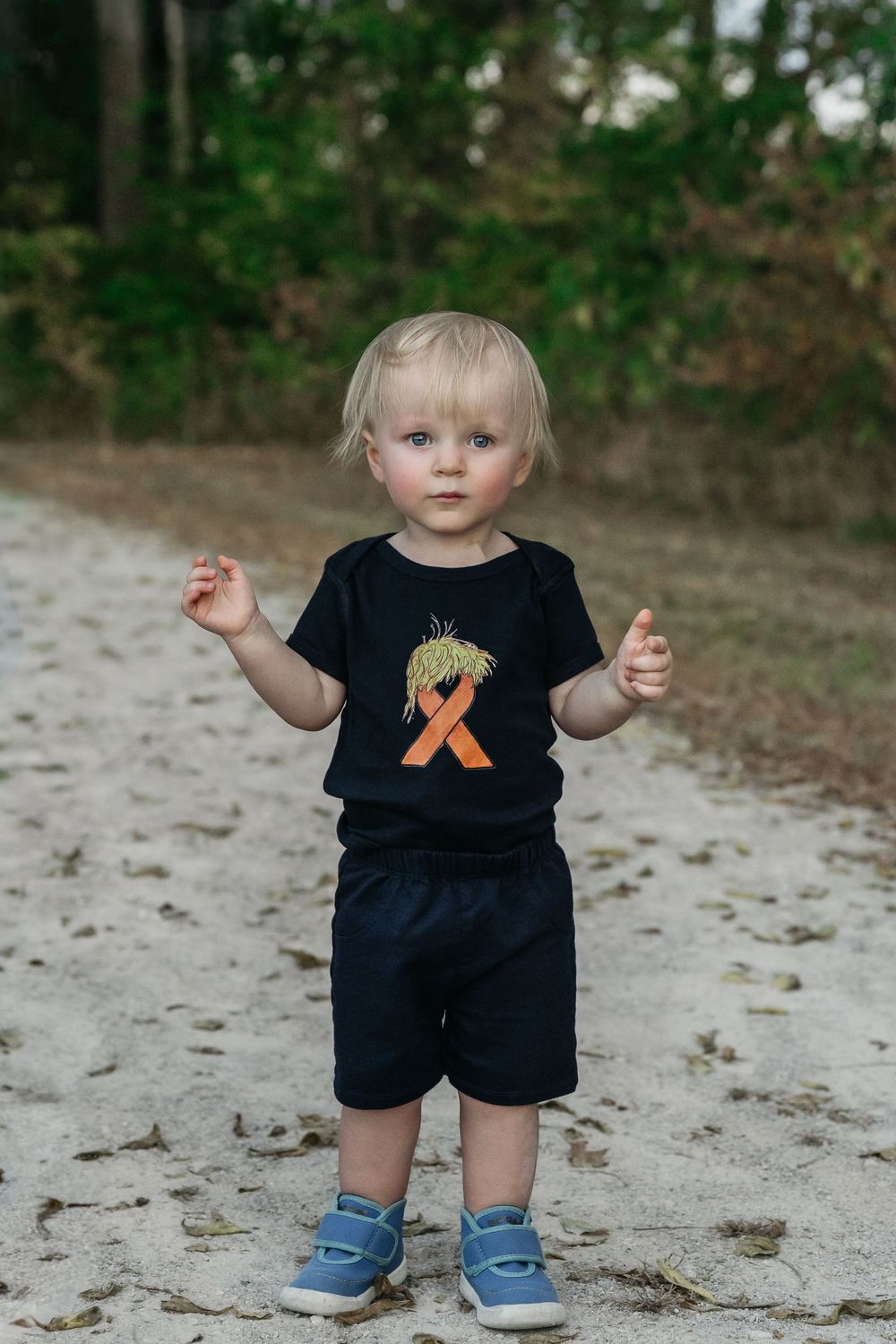 Small child wearing a black t-shirt and shorts stands on a path covered with fallen leaves for Delaware, Ohio family photos