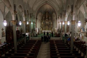 Interior of gothic cathedral with vaulted ceilings and ornate altar in dim lighting.