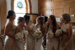 Row of bridesmaids in formal dresses holding matching bouquets in rustic wooden venue.