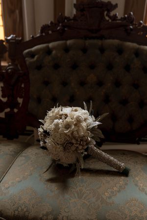 Wedding bouquet with white roses and feathers resting on a tufted blue fabric surface.