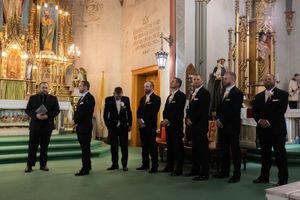 Wedding party members in formal black attire lined up in a church sanctuary.