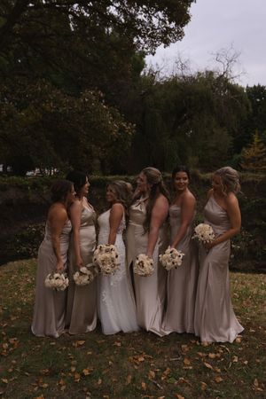 Bridesmaids in matching champagne dresses pose with bouquets in an autumn garden setting.