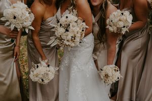 Wedding party members hold elegant white floral bouquets against neutral colored attire.