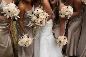 Bridesmaids in champagne dresses holding white and cream floral bouquets.