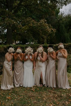 Wedding party poses playfully hiding behind white bouquets in an autumn setting.