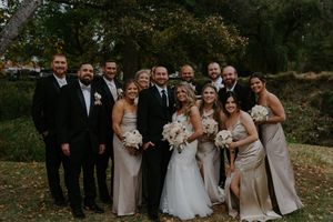 Wedding party stands together outdoors during fall with trees in background.