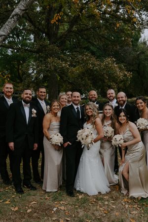 Large wedding party poses together on autumn grounds with fallen leaves.