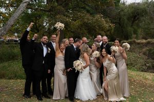 Wedding party celebrating outdoors with raised arms and bouquets against autumn trees.