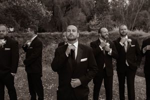 Groomsmen in black suits posing together outdoors for formal wedding photos.