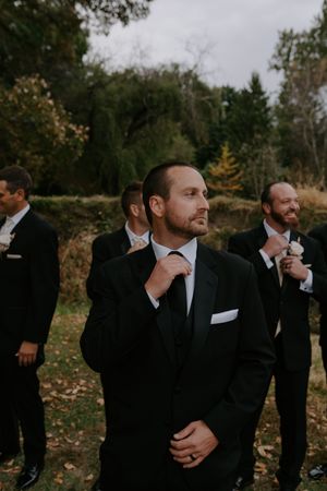Groomsmen in dark suits and ties look away from camera in artistic wedding photo.