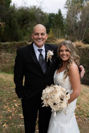Bride in white lace gown holds cream bouquet while posing for outdoor autumn wedding photos.
