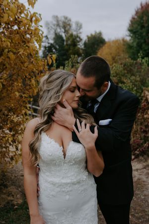 Intimate wedding couple shares romantic moment against autumn foliage backdrop in formal attire.