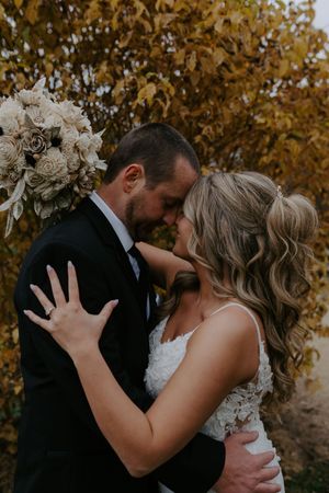 Newlyweds embrace tenderly during outdoor fall photo session with golden leaves.