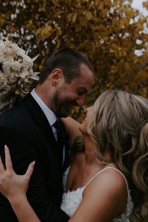 Close-up of romantic wedding moment with couple kissing among autumn trees.