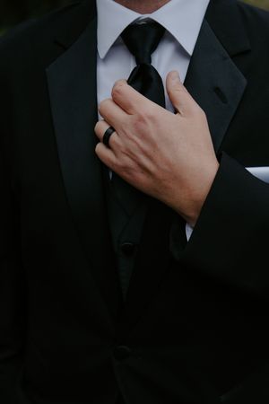 Close-up detail of groom adjusting black tie and formal attire.