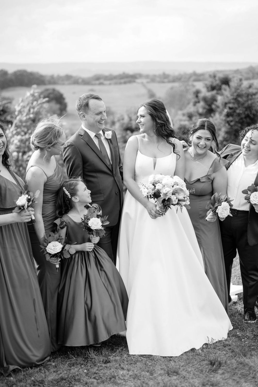 Wedding party in gray dresses and formal attire gathered outdoors for group photos.