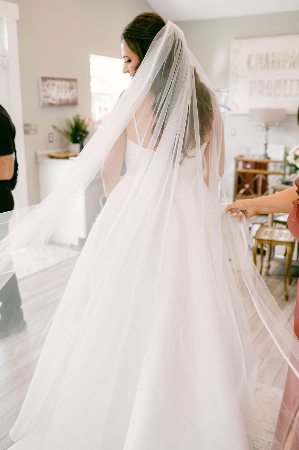 Flowing white wedding dress with veil being fitted in a bright bridal boutique.