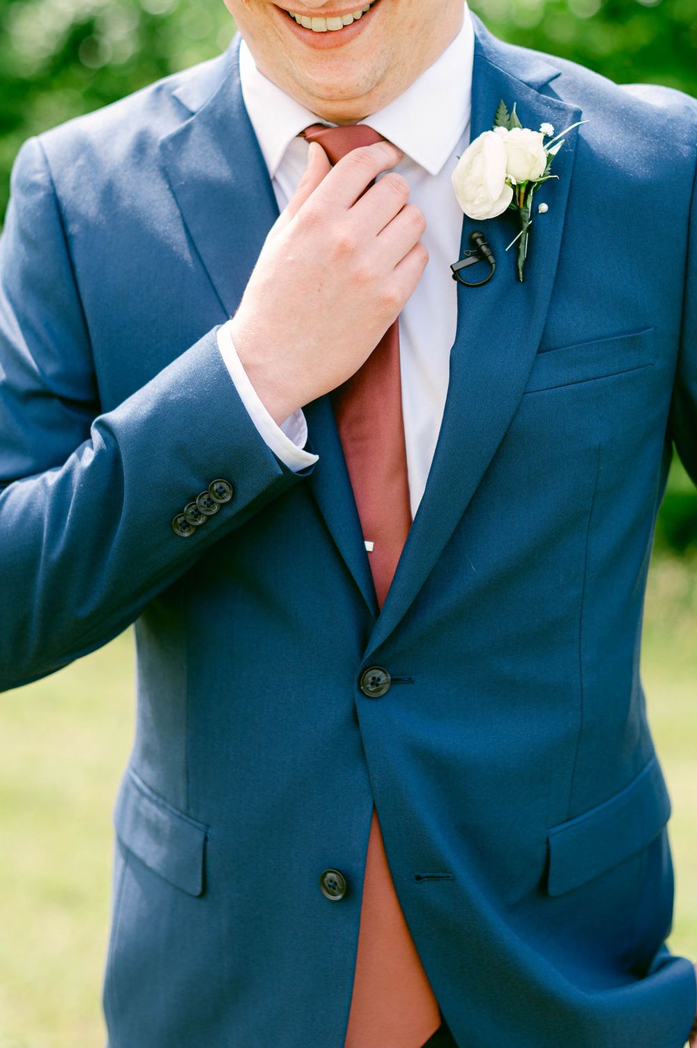 Detail shots of groom adjusting tie and boutonniere while wearing navy suit with coral tie.