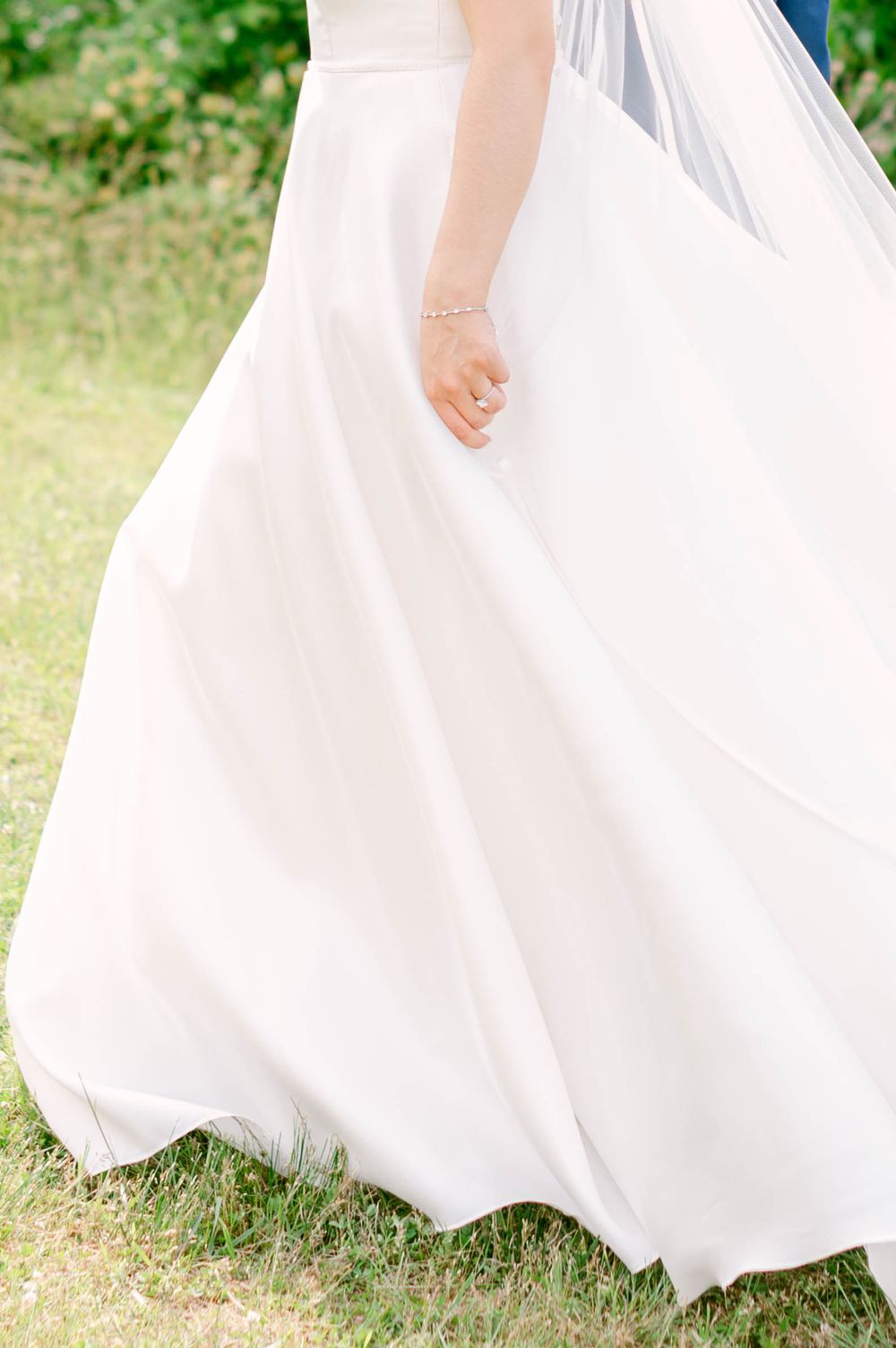 Close-up view of flowing white wedding dress fabric swaying gracefully against a green outdoor background.