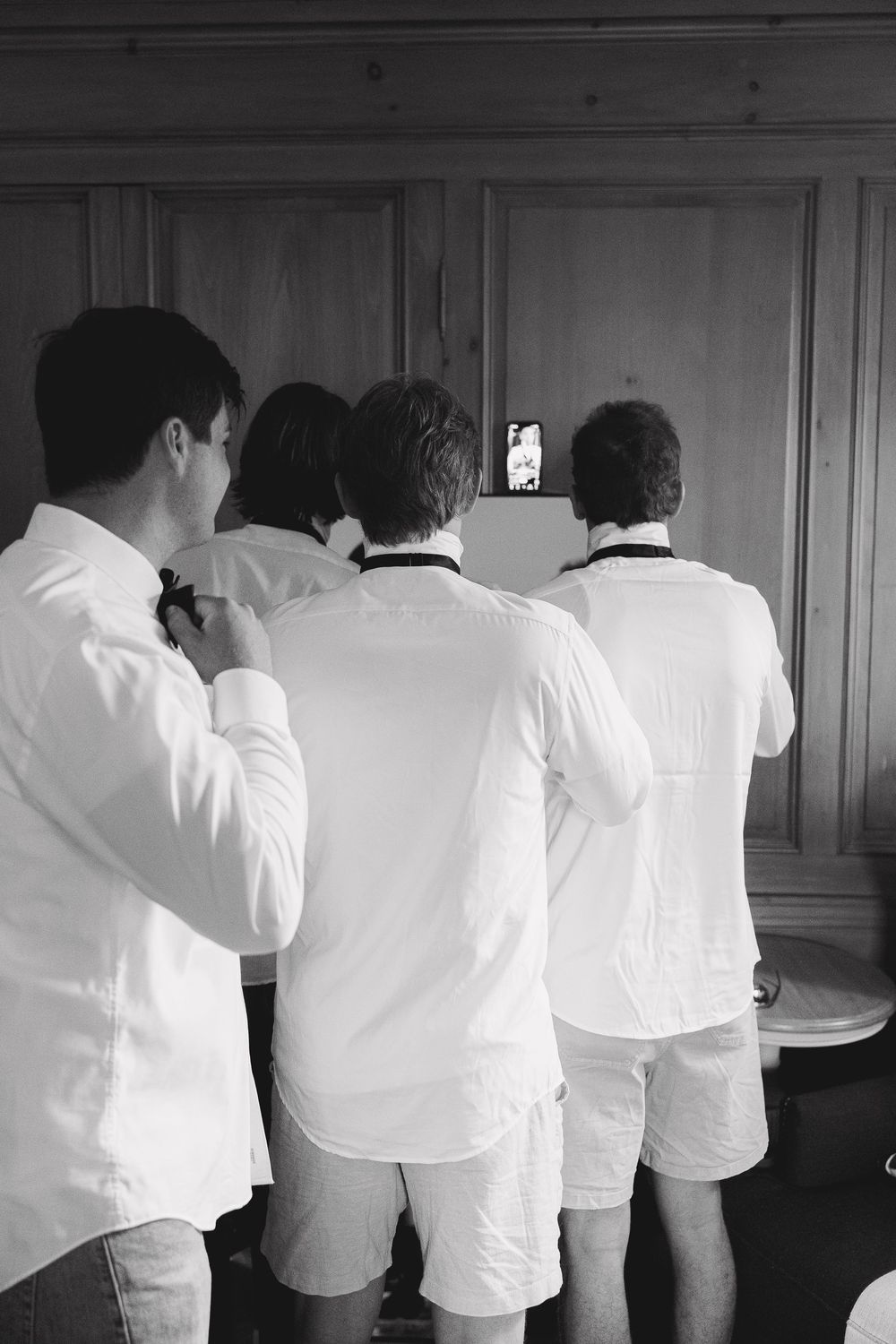 Black and white photo of groomsmen in white shirts preparing for a wedding ceremony.