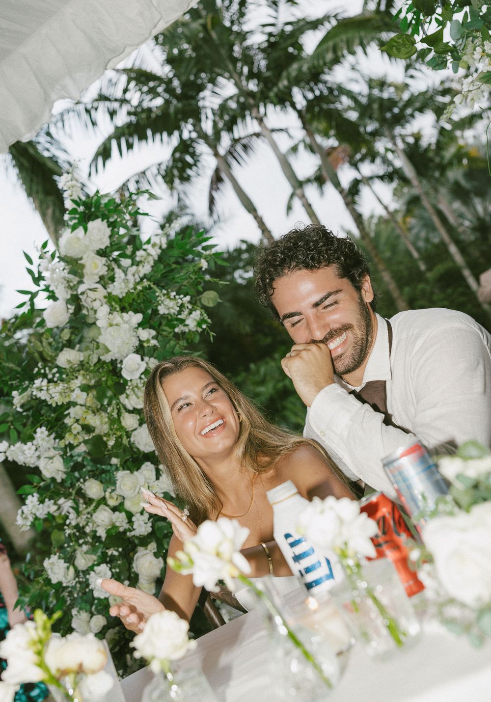 Wedding party members laugh and celebrate at outdoor tropical reception.