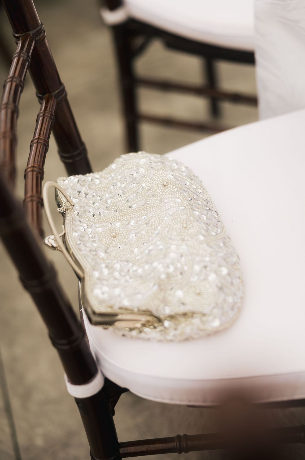 Elegant beaded white clutch purse with sequins resting on a white chair at a wedding reception.