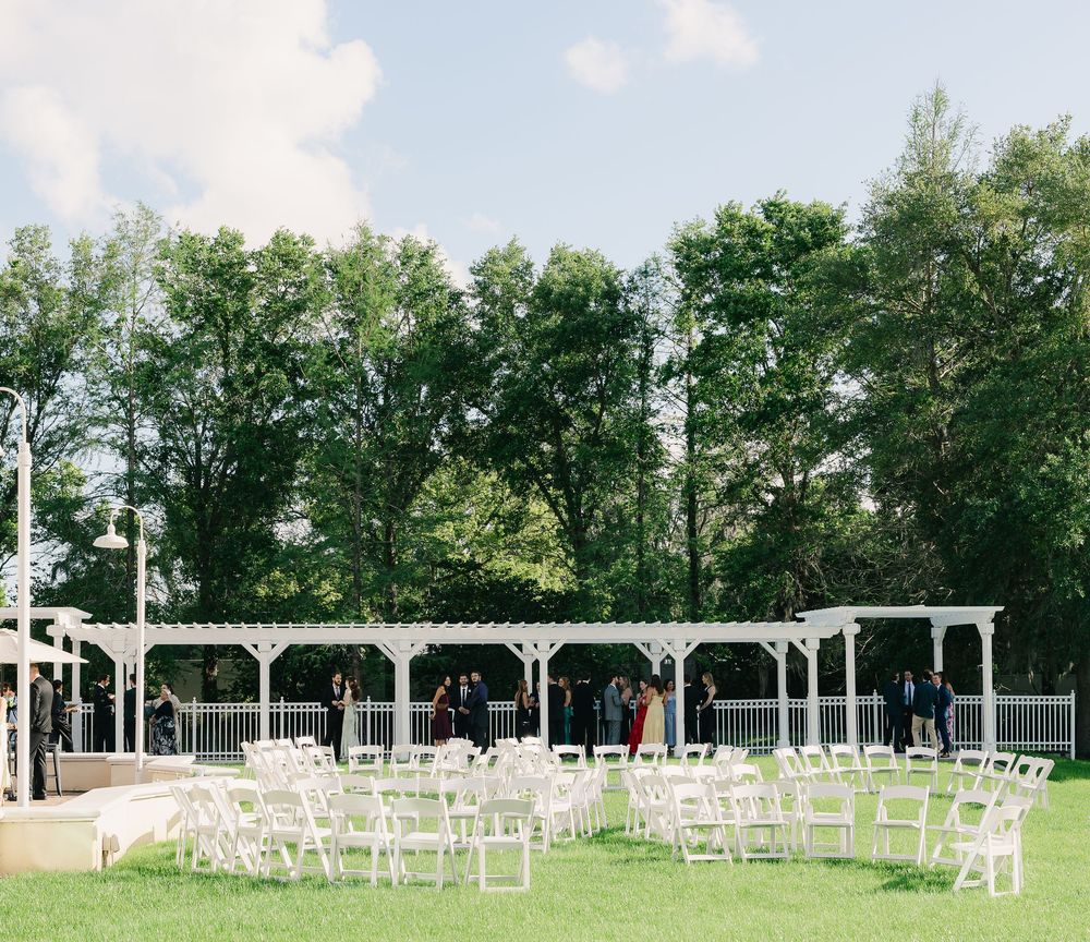 Outdoor wedding ceremony setup with white chairs on green lawn under a white pergola.
