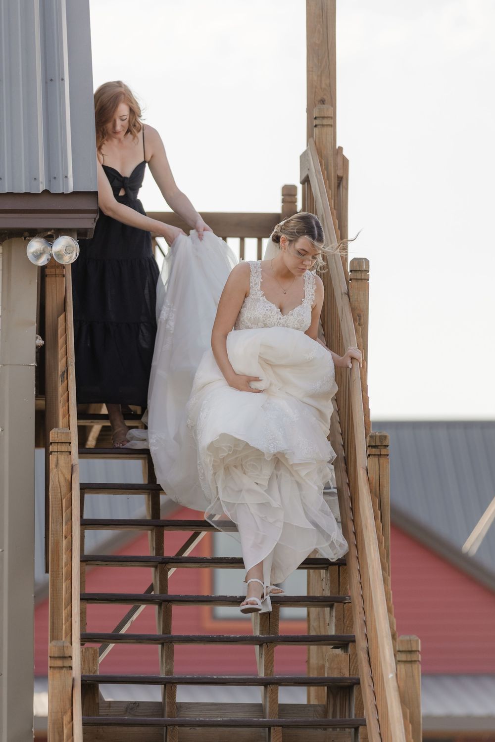 A bride in a flowing white dress sits elegantly on wooden stairs during a wedding photoshoot.
