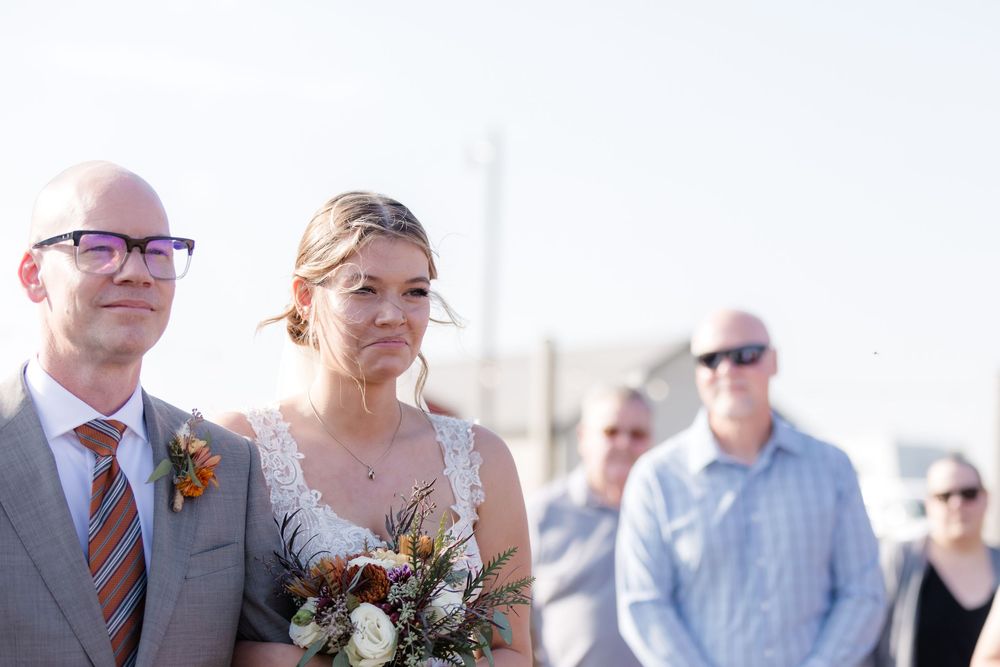 Wedding guests mingle and socialize at an outdoor reception under bright sunlight.